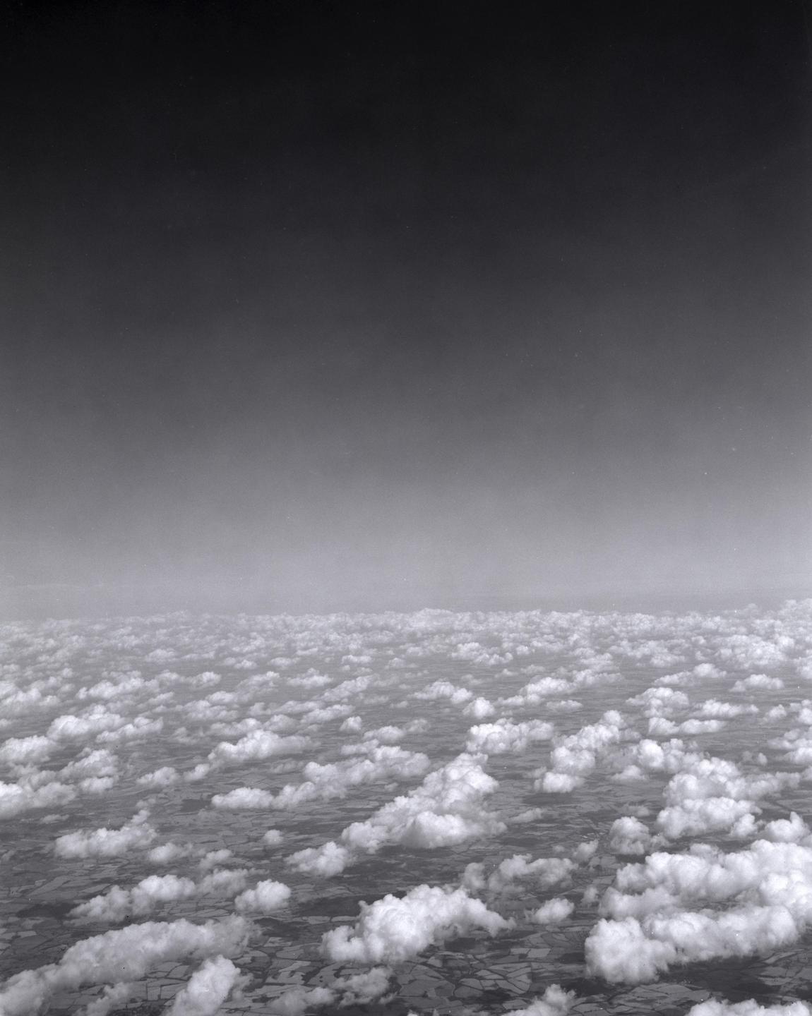 An aerial view shows a vast expanse of clouds floating above a patchwork of fields.