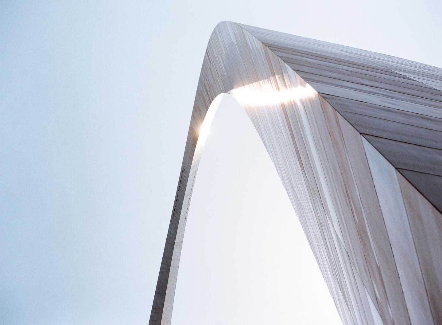 The Gateway Arch in Saint Louis is shown from a low angle with the sun flaring through the archway.