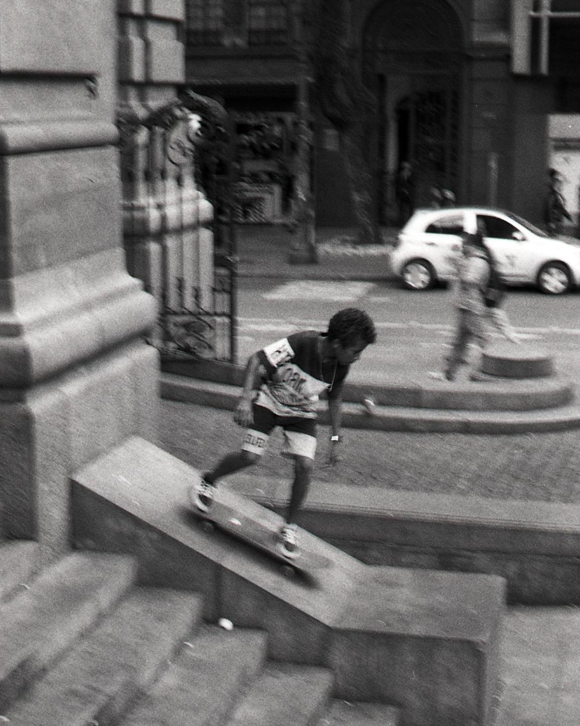 A boy on a skateboard rides down a concrete ramp on a city street.