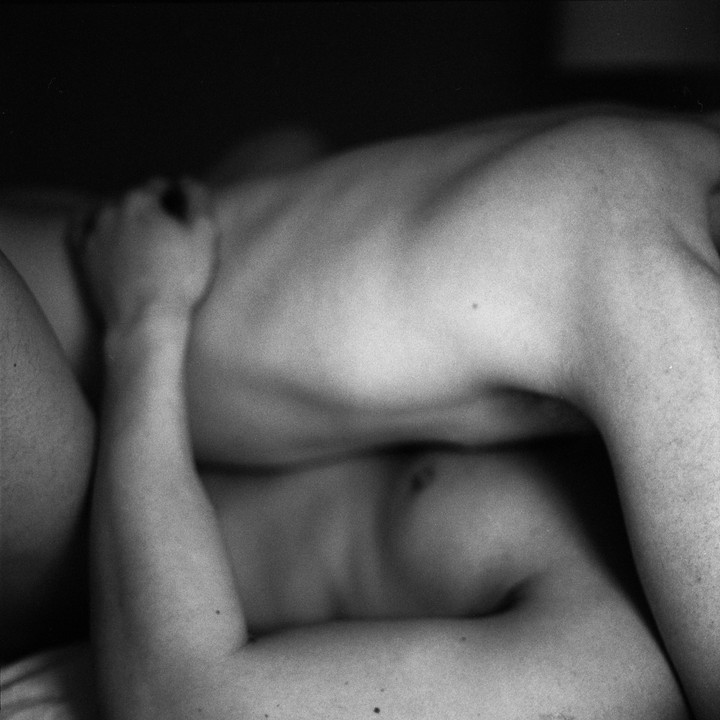 Two shirtless people are embracing in a close-up, intimate shot.