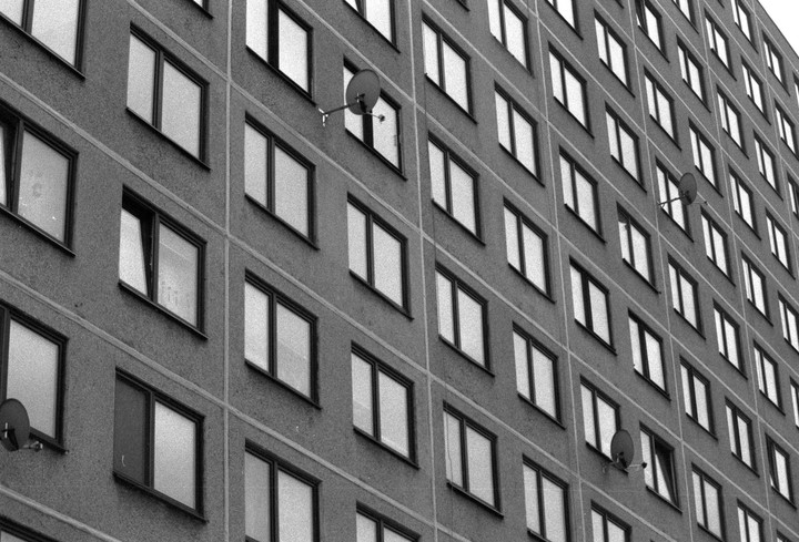 A tall building with many windows and a few satellite dishes is shown from a low angle.
