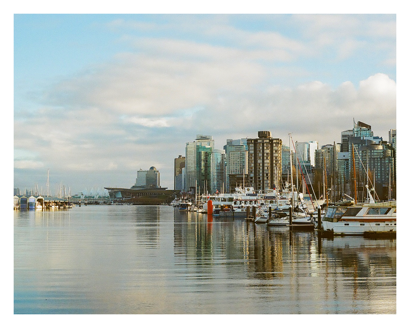 A body of water with boats and a city skyline with tall buildings under a cloudy sky.