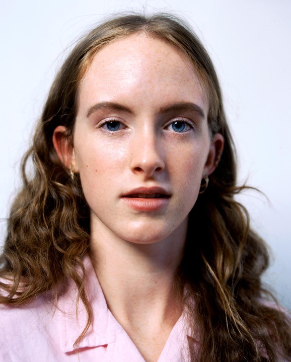A young woman with long wavy hair and blue eyes looks directly at the viewer.