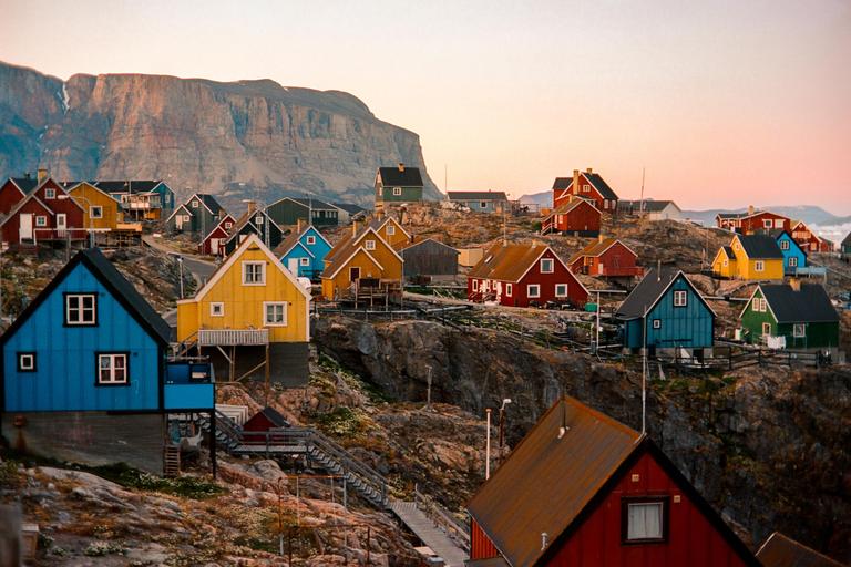 A village of colorful houses is built into a rocky hillside with a large mountain in the background.
