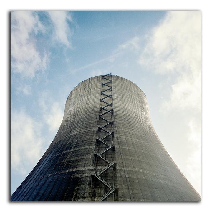 A large cooling tower with a zig-zagging ladder on its side stands against a cloudy sky.