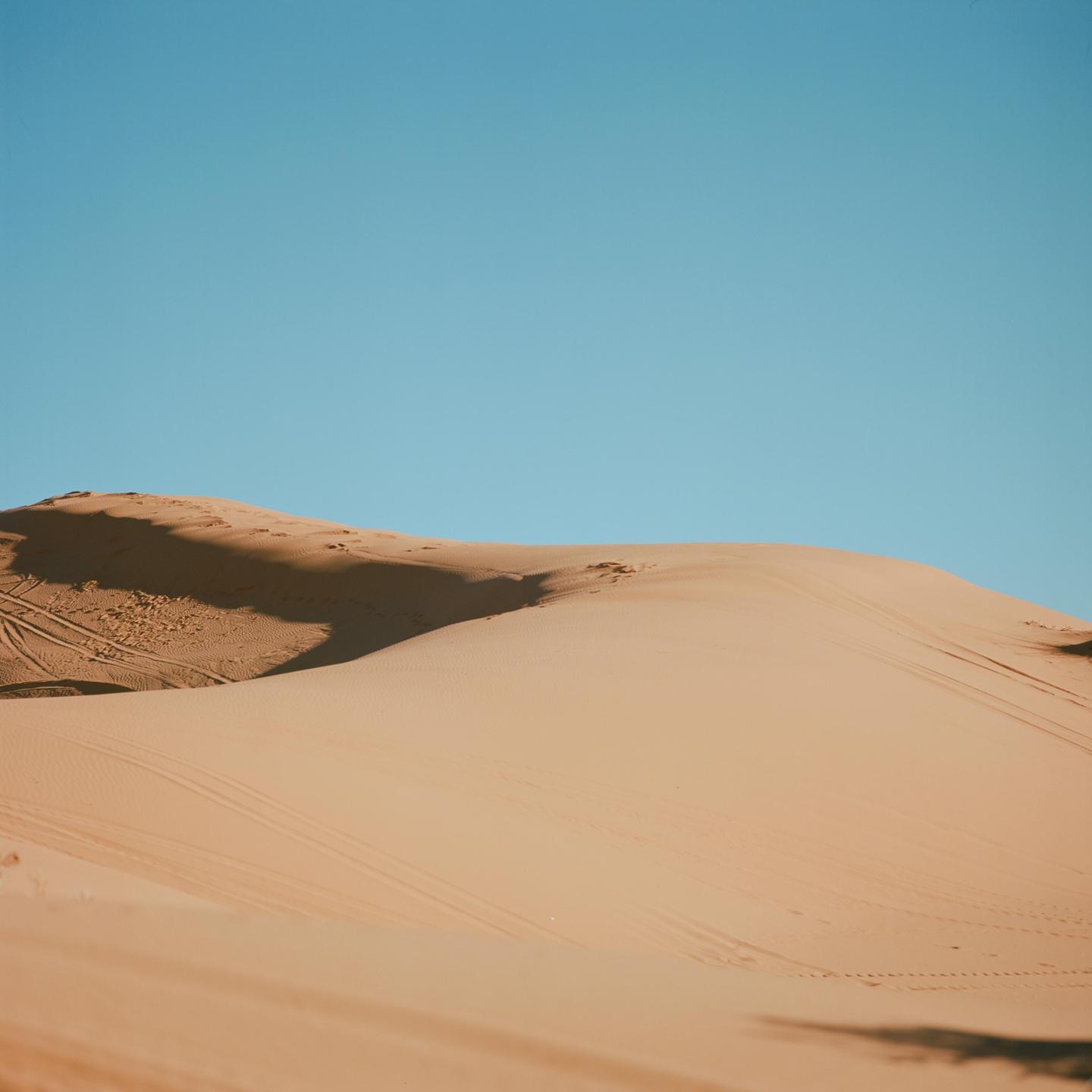 A large sand dune casts a shadow under a clear blue sky.