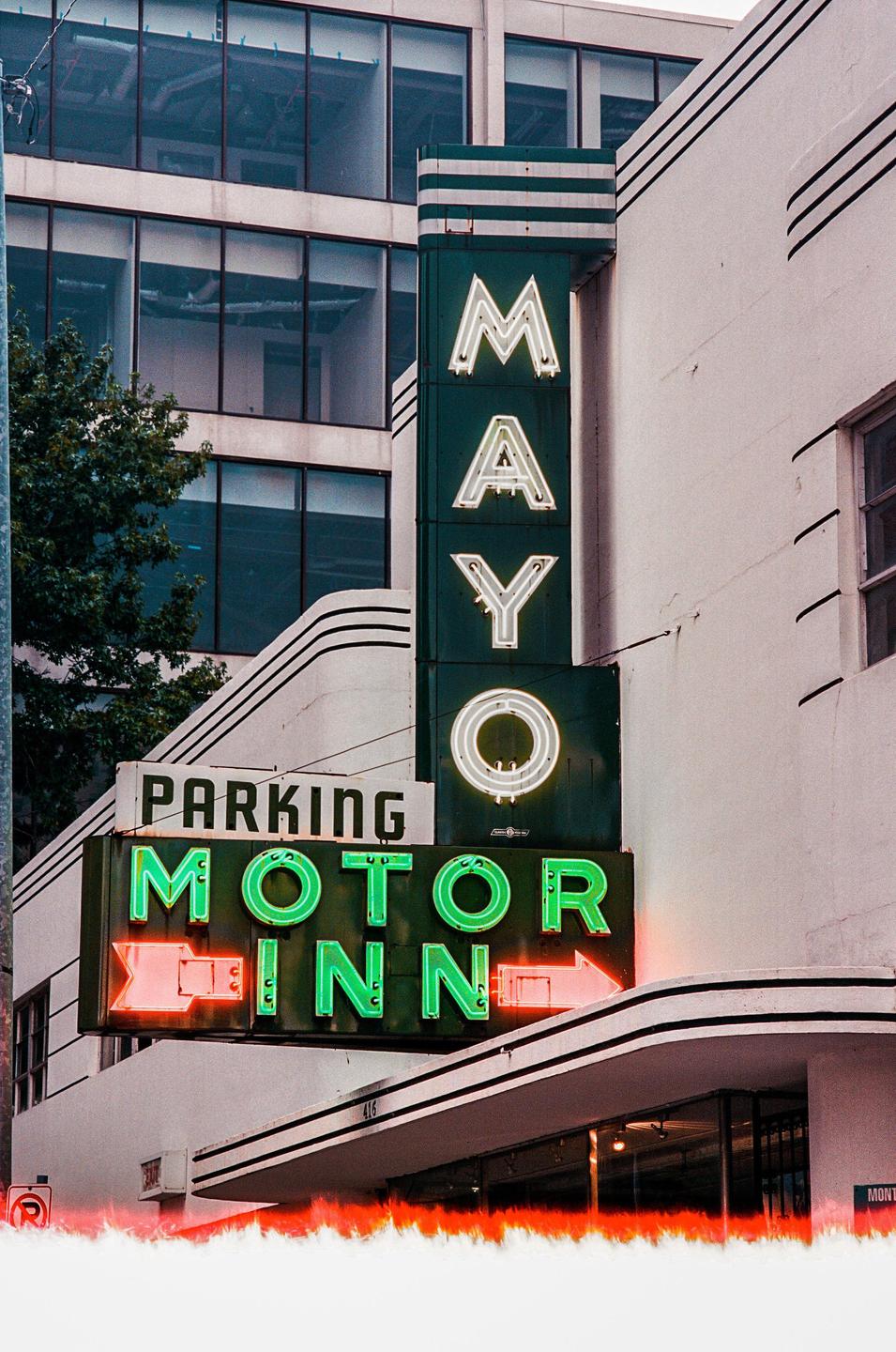 A neon sign for the Mayo Motor Inn is attached to a white building with black stripes.