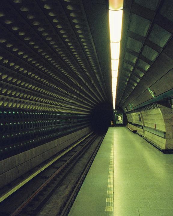 A long, empty subway platform stretches into the distance, illuminated by a single strip of light on the ceiling.