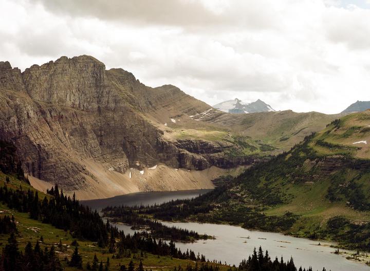 A wide mountain valley with a lake and evergreen trees is visible under a cloudy sky.