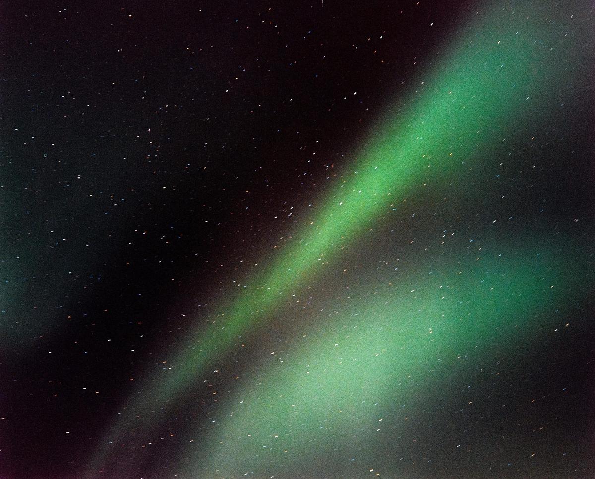 The aurora borealis glows green in the night sky above a scattering of stars.