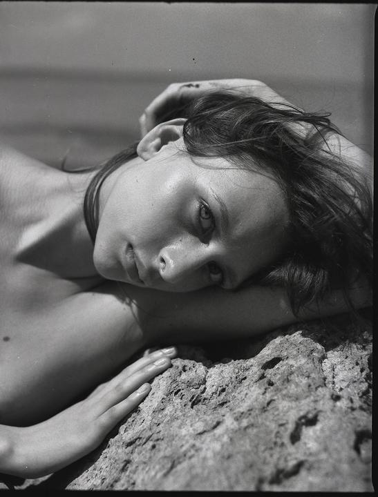 A woman with dark hair is lying on a rock, looking towards the viewer.