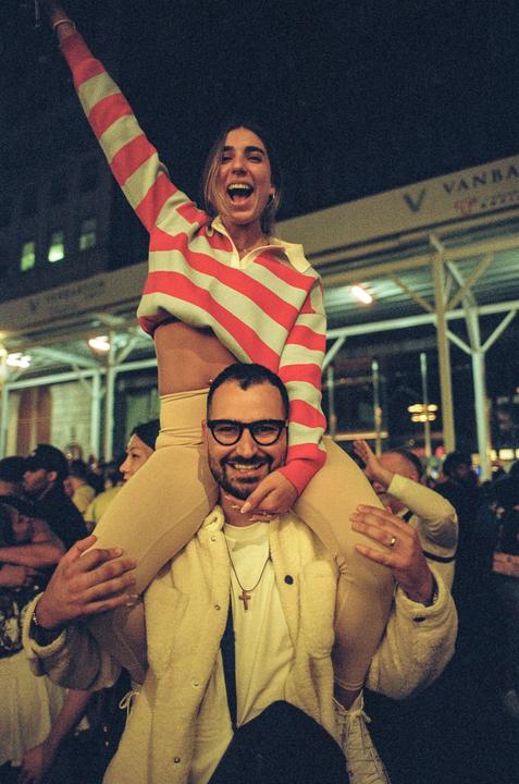 A man carries a woman on his shoulders in a crowd at night.
