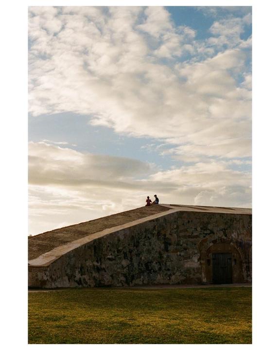 Two people sit atop a stone wall under a cloudy sky.