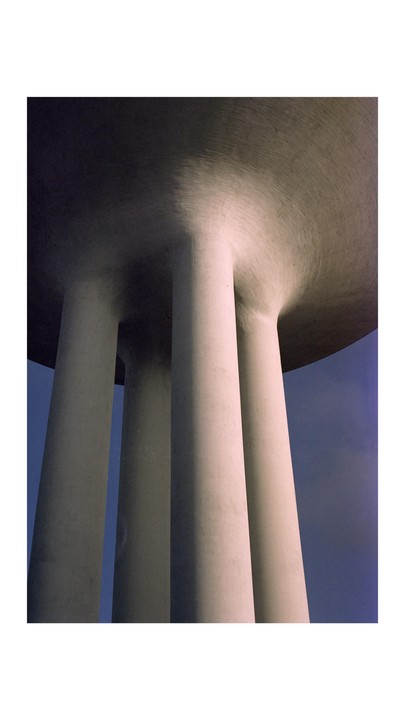 A low-angle view shows the concrete pillars supporting a large, round structure against a blue sky.