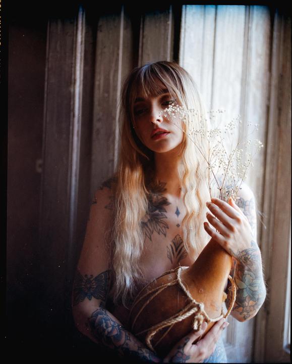 A woman with long blonde hair and tattoos holds a gourd and dried flowers.