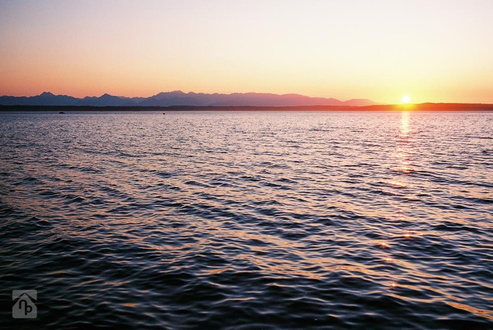 The sun sets over a body of water with mountains in the distance.