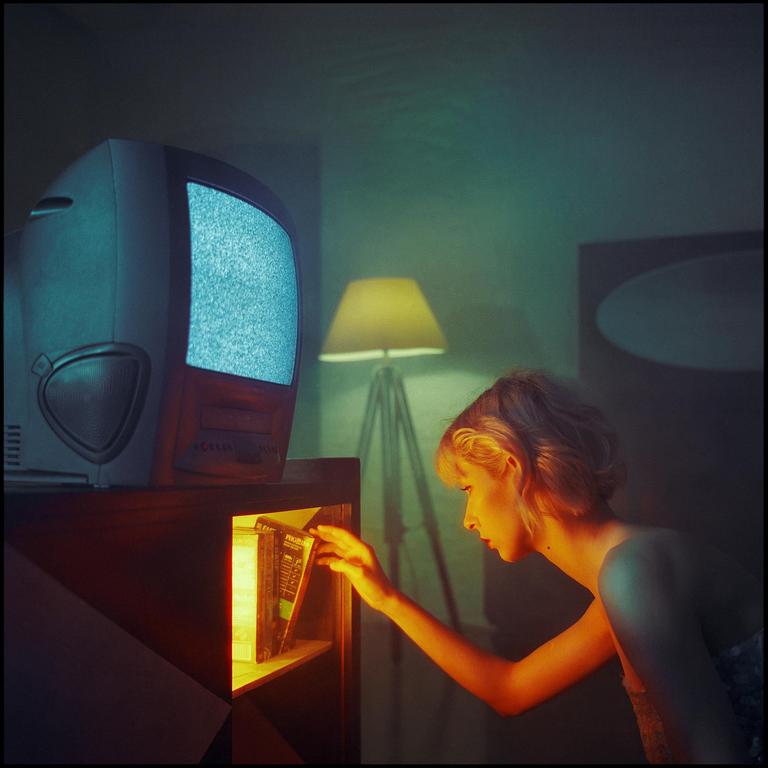 A woman reaches for a book on a shelf next to a television with a static screen.