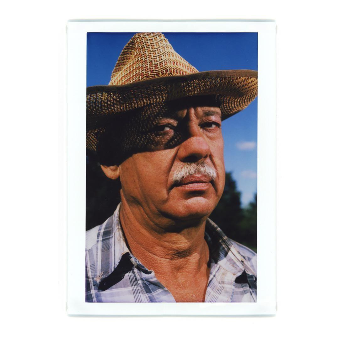 A man wearing a straw hat and a plaid shirt looks directly at the viewer.