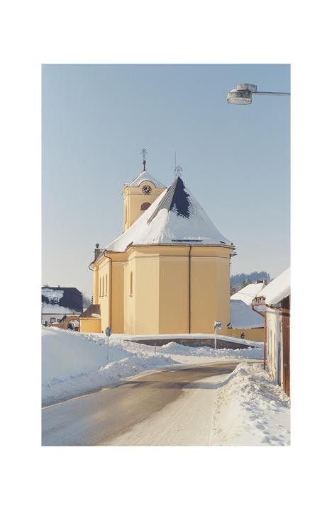 A yellow church with a snow-covered roof stands beside a snowy road under a clear sky.