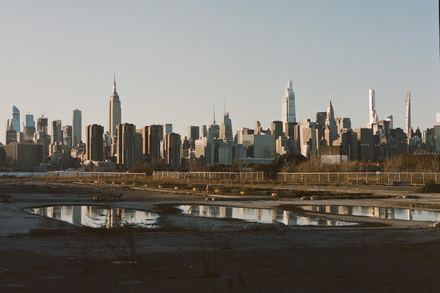 A cityscape with skyscrapers is reflected in puddles on the ground.