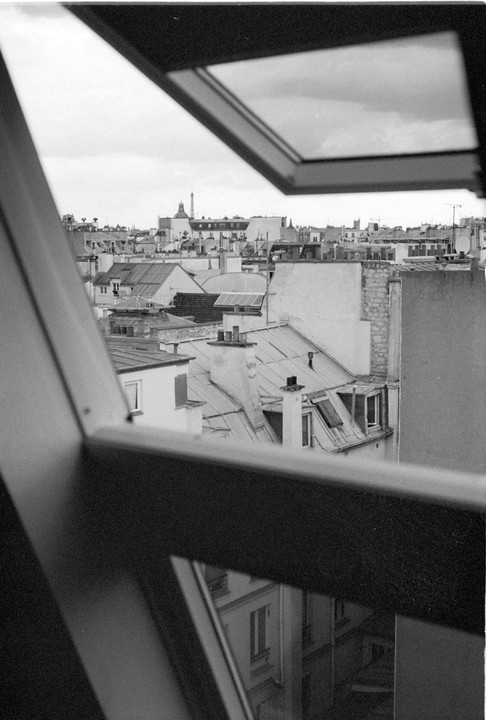 A view of Parisian rooftops and the Eiffel Tower in the distance is framed by an open window.