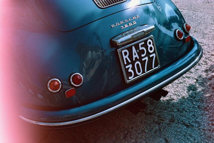 The rear of a blue Porsche 1600 is visible with a license plate and taillights.