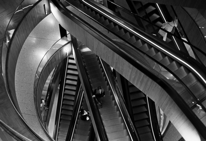 A woman and a man ride escalators in a modern building with curved walls.