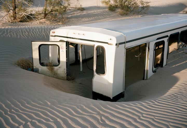 A white vehicle is half-buried in sand dunes with its doors open.