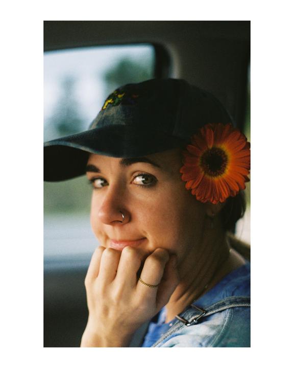 A woman wearing a baseball cap with a flower tucked into it looks over her shoulder.