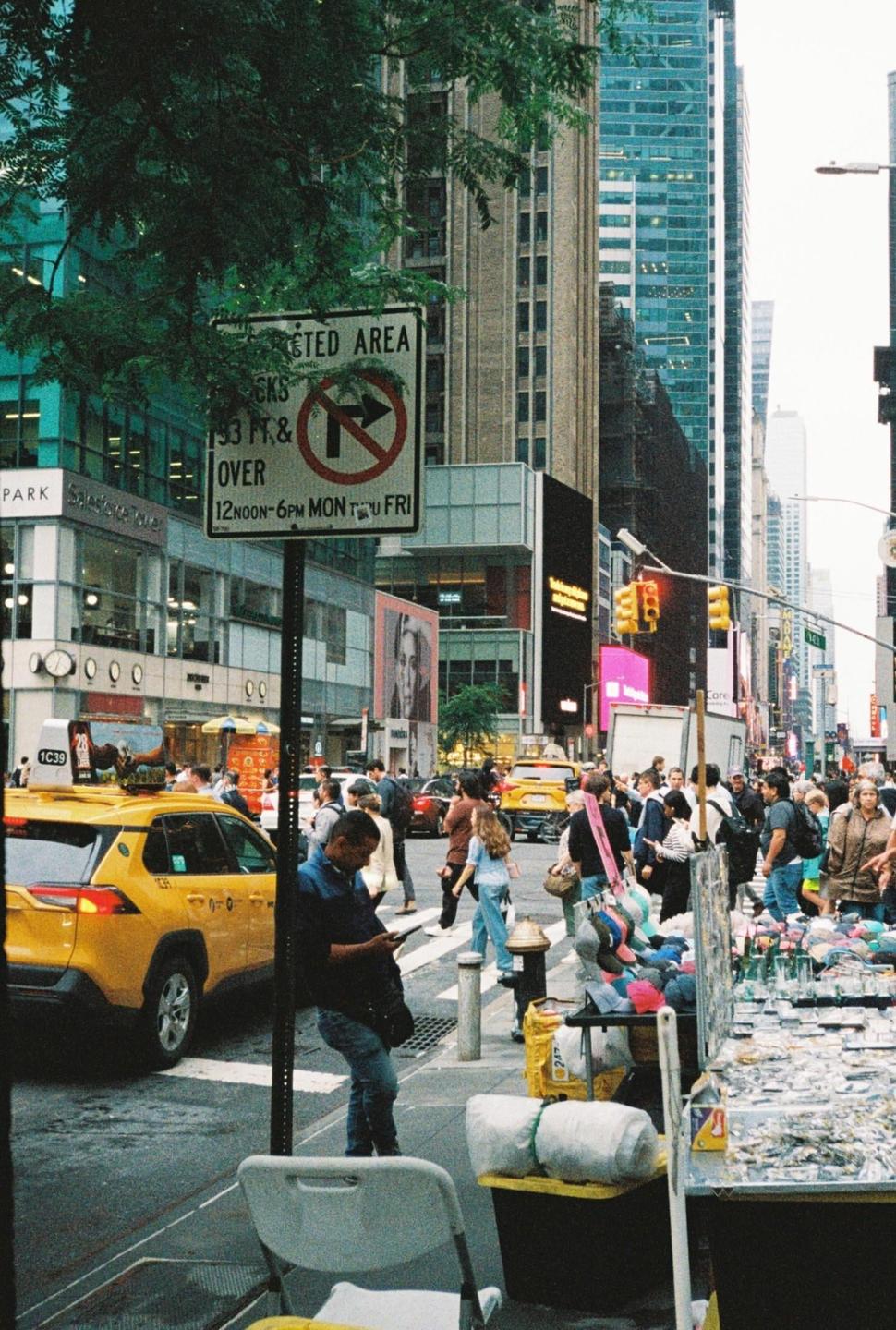 A busy street in New York City is filled with pedestrians, yellow taxis, and tall buildings.