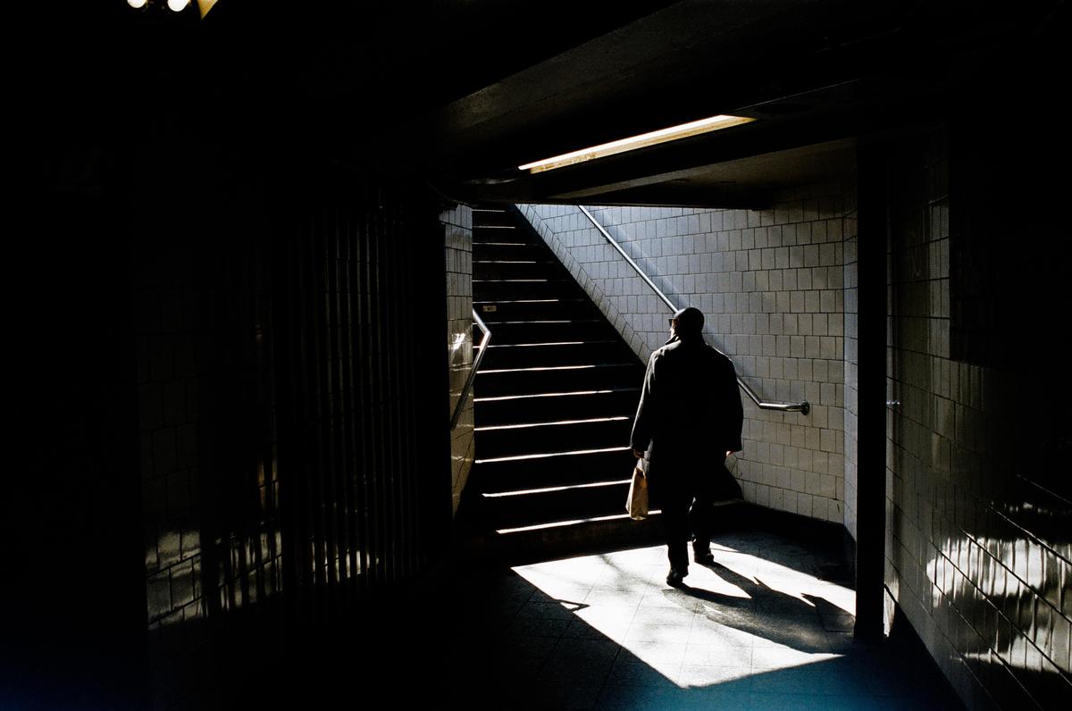 A man walks up a subway staircase with light and shadow creating a dramatic effect.