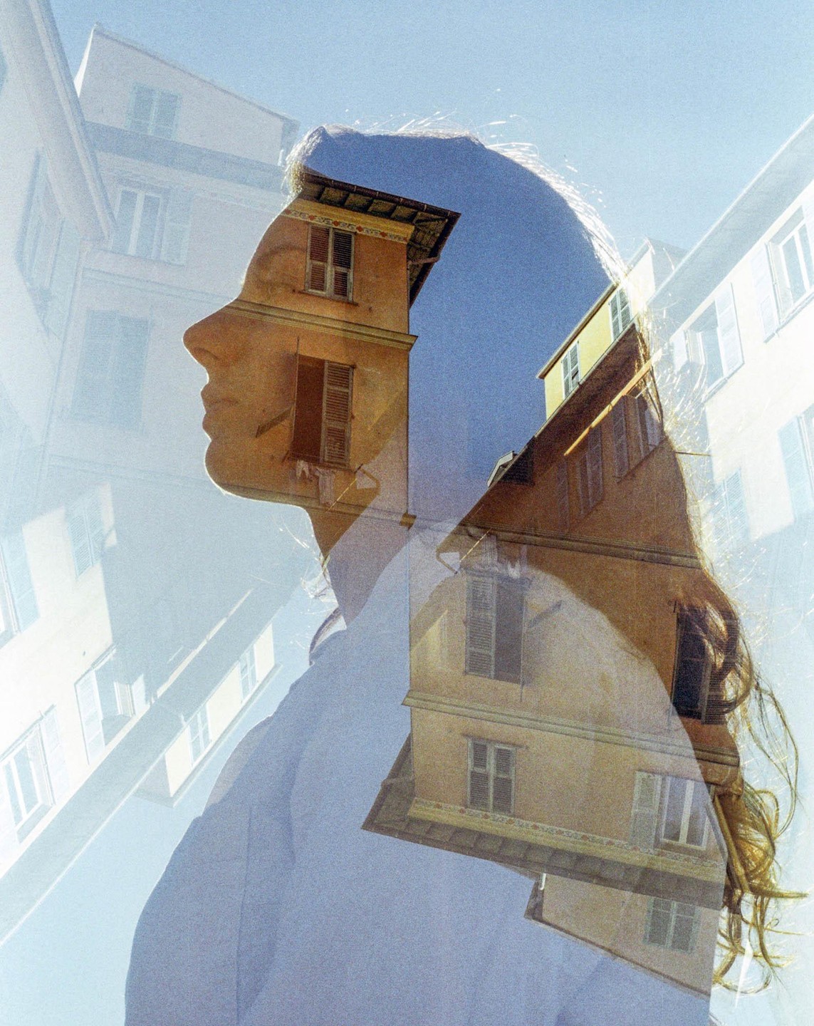 A woman's profile is superimposed with multiple exposures of building facades under a clear sky.