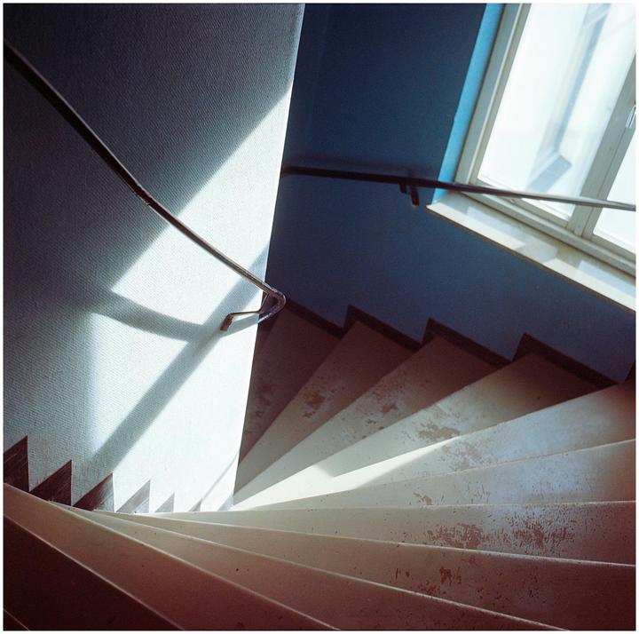 Sunlight streams through a window onto a stairwell with a handrail.