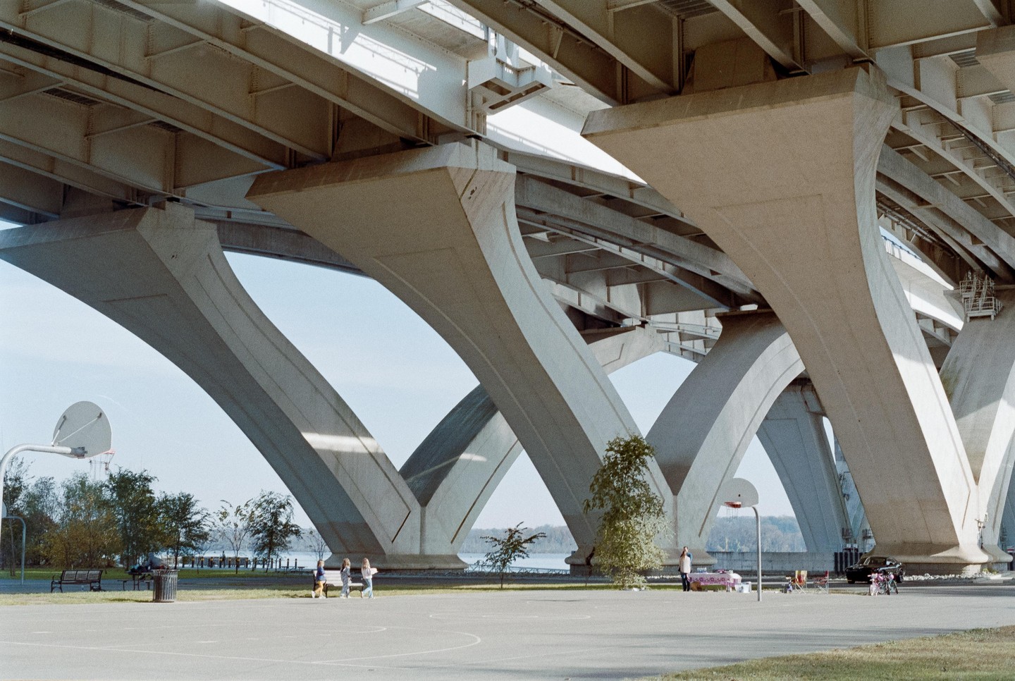 A wide shot shows the underside of a large concrete bridge with multiple arches, under which a basketball court and several people are visible.