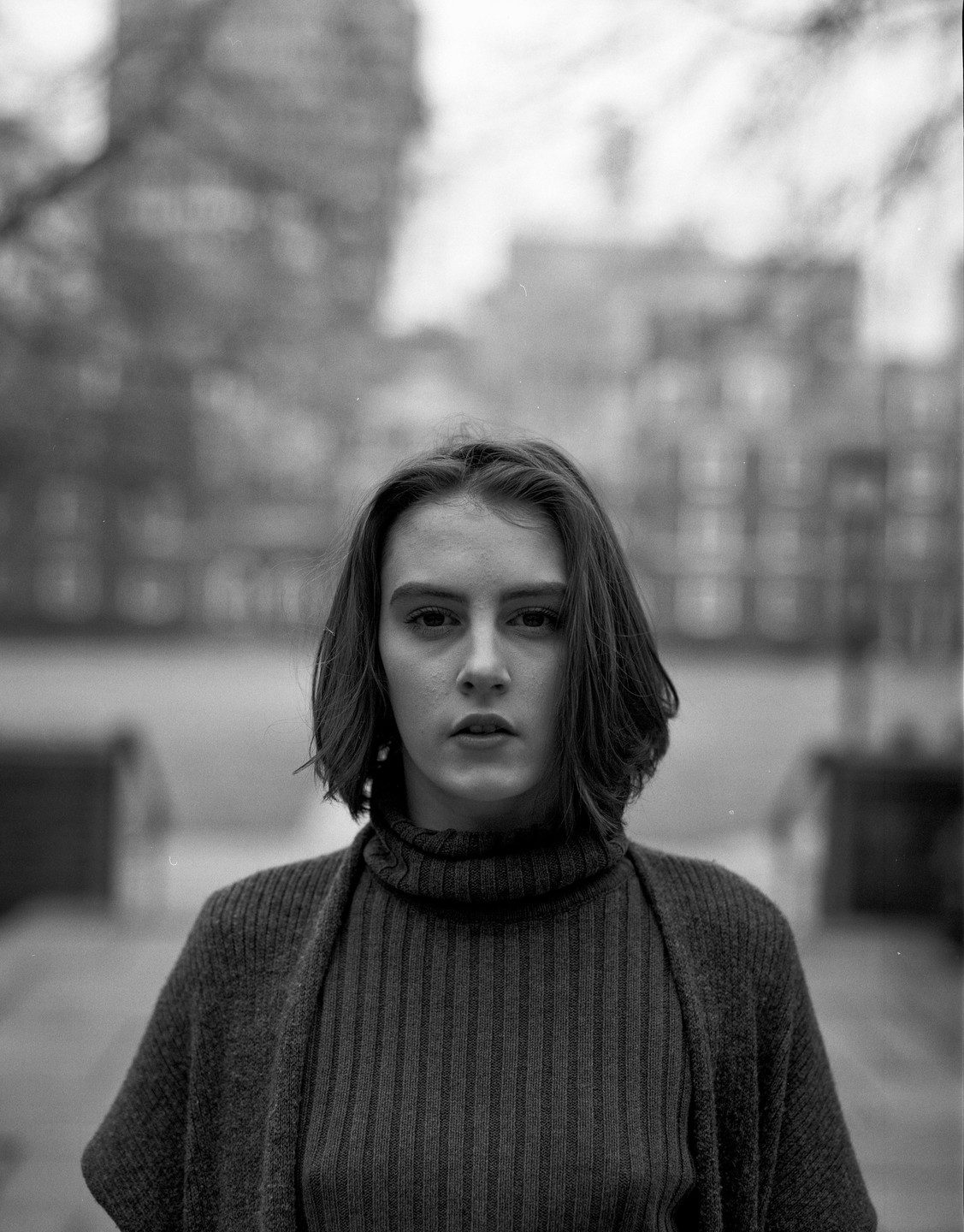 A woman with short hair and a turtleneck sweater looks directly at the viewer.
