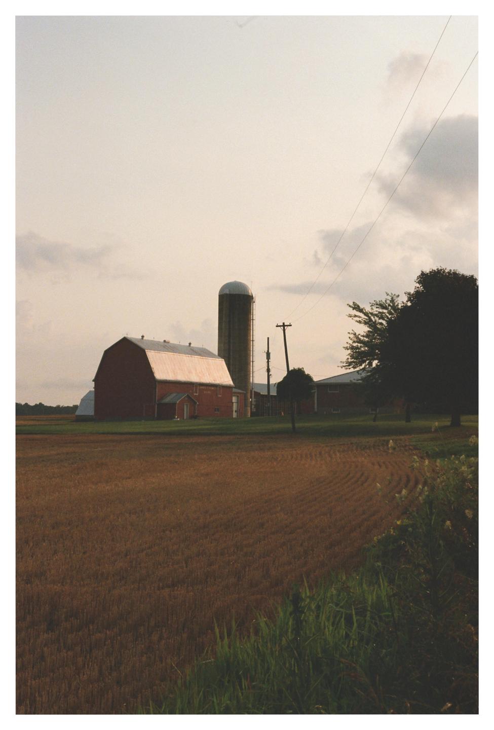 A red barn and silo stand in a field under a cloudy sky.