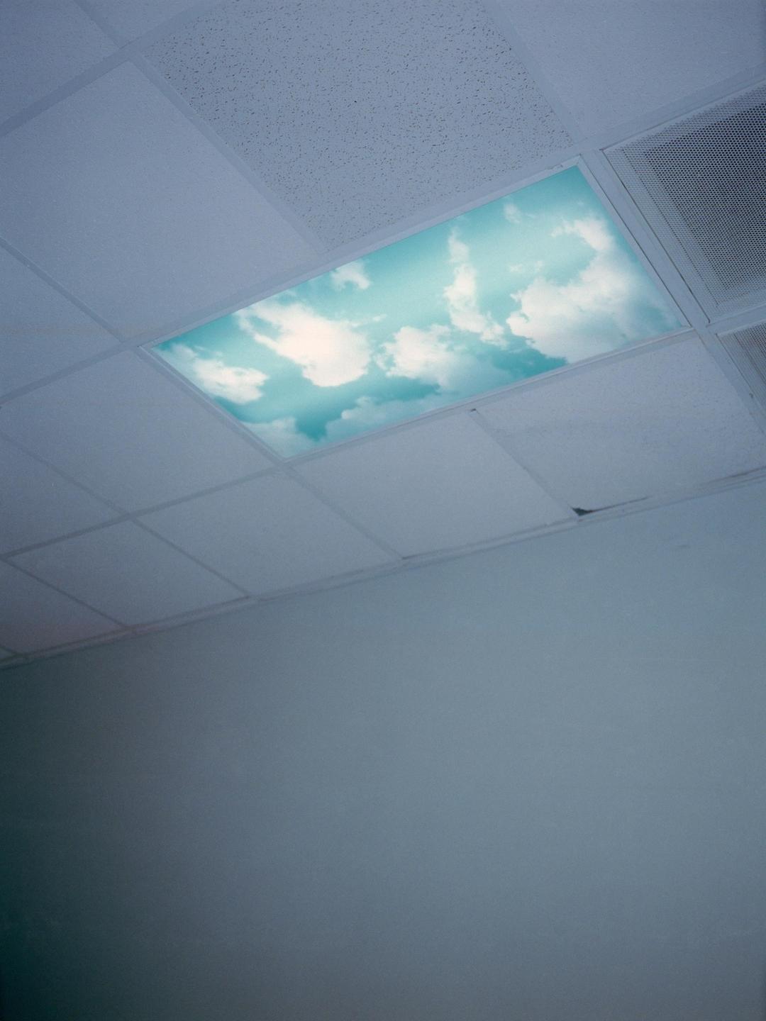 A ceiling panel with a sky and clouds design is visible in a room with a plain wall.
