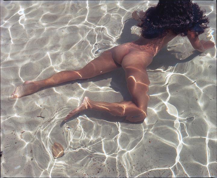 A woman is submerged in clear, shallow water with sunlight reflecting on the surface.