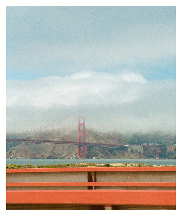 The Golden Gate Bridge is partially obscured by fog, with a red barrier in the foreground.