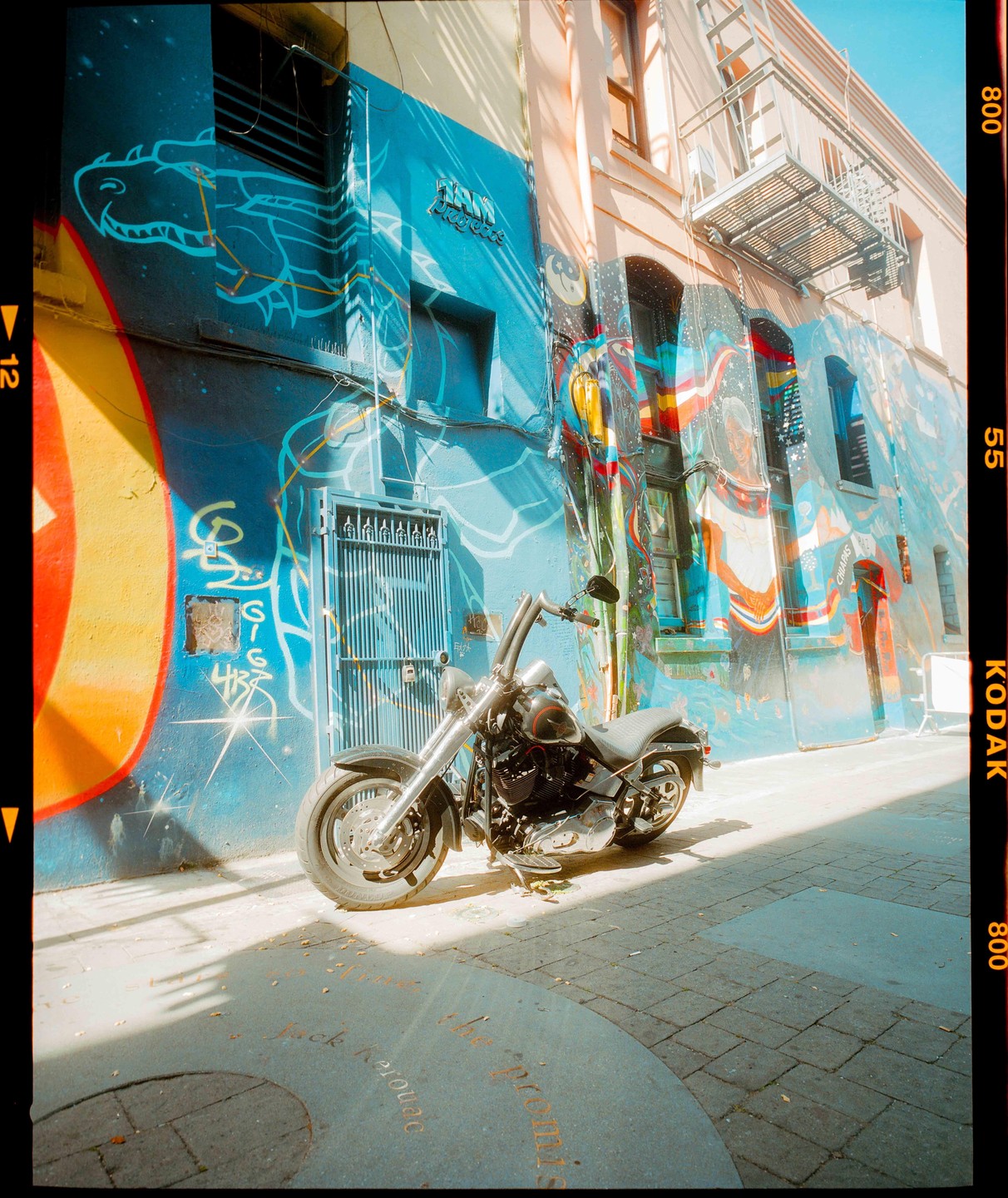A motorcycle is parked on a street next to a building covered in colorful murals and graffiti.