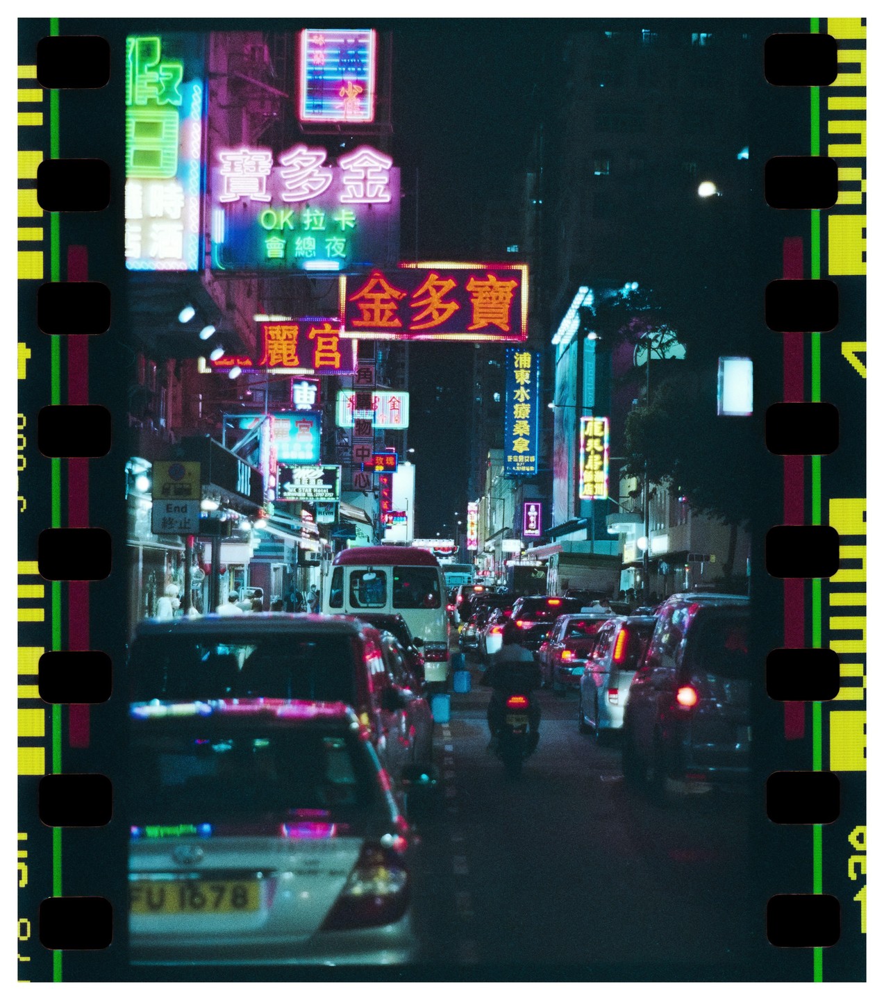 A busy street at night is filled with cars, a motorcycle, and neon signs.