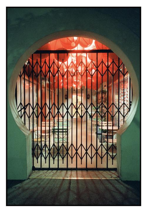 A closed gate with a pattern of red lanterns visible through it.