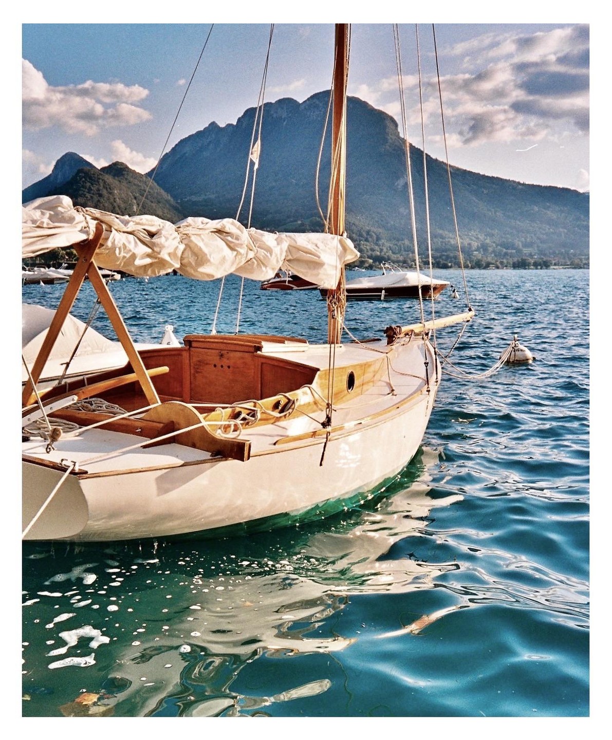 A sailboat is moored on a lake with mountains in the background.