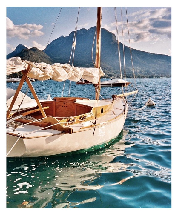 A sailboat is moored on a lake with mountains in the background.