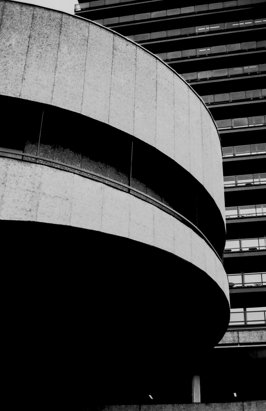 A curved concrete building facade with dark shadows is shown next to a building with many balconies.