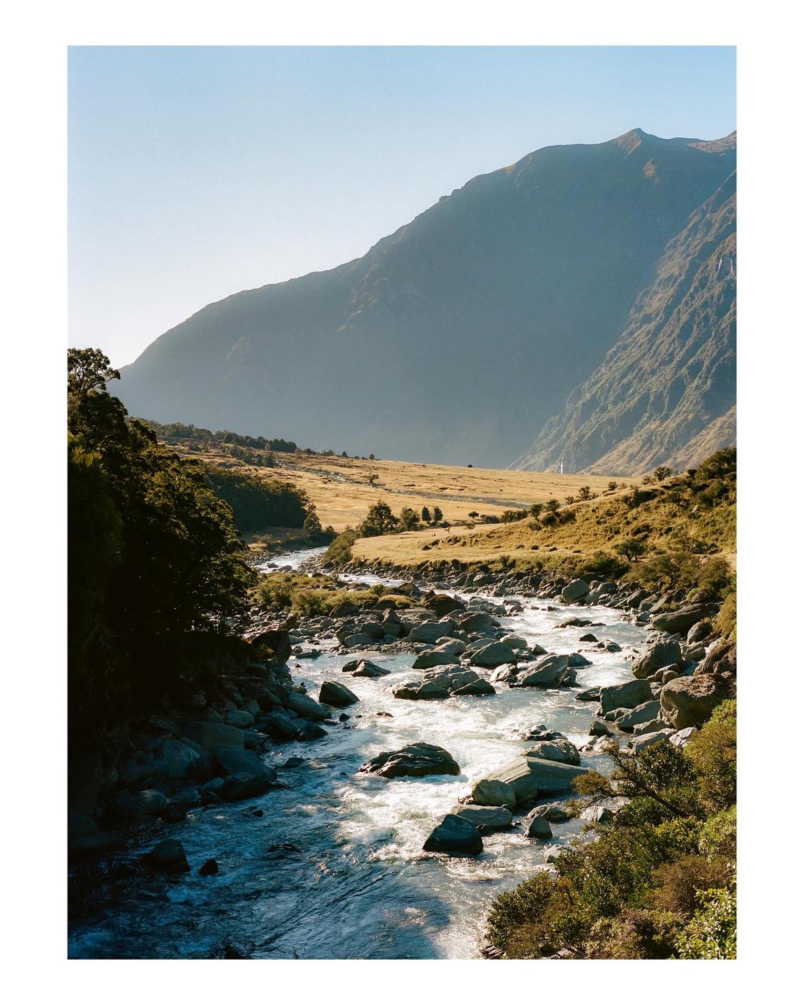 A river with many rocks flows through a valley with mountains in the background.
