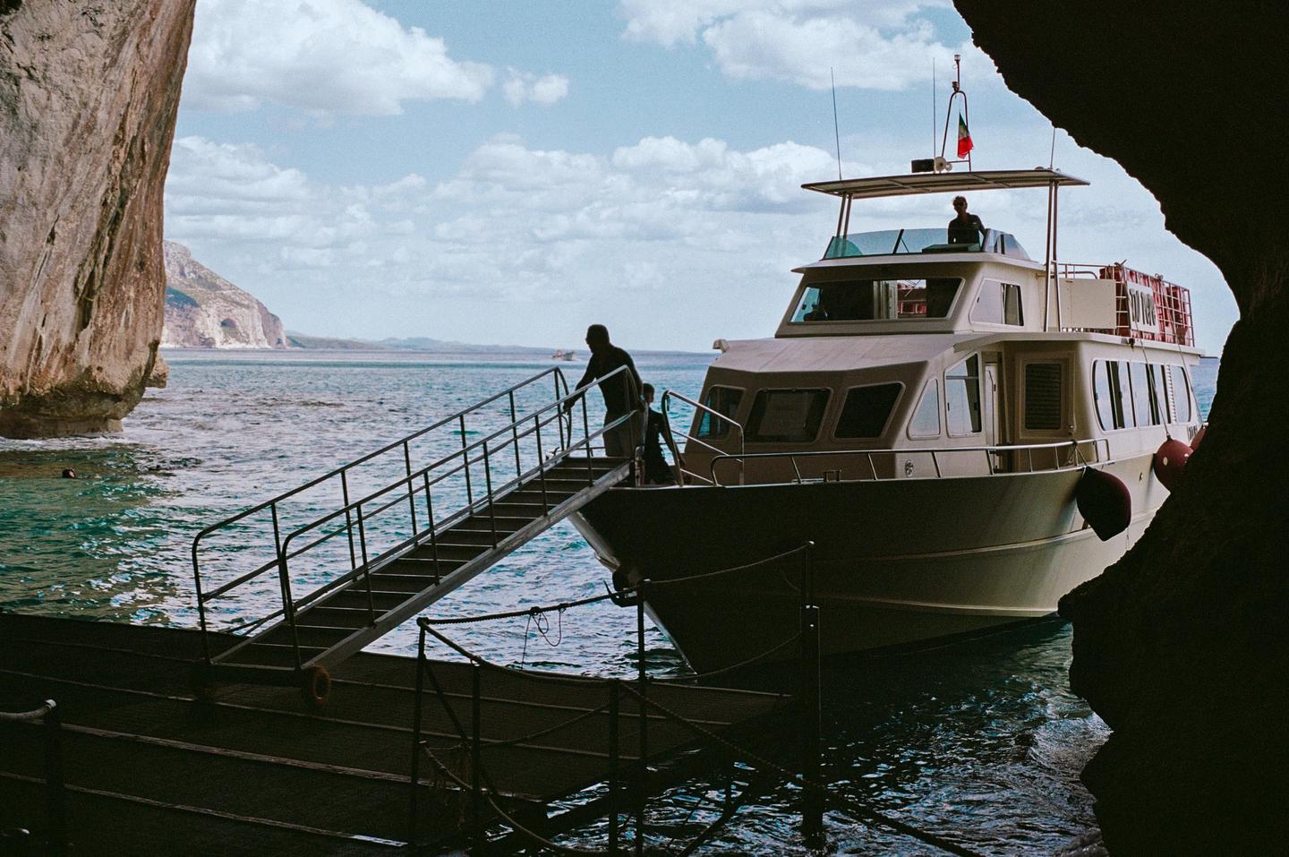 A boat is docked at a rocky shore with people disembarking onto a gangway.