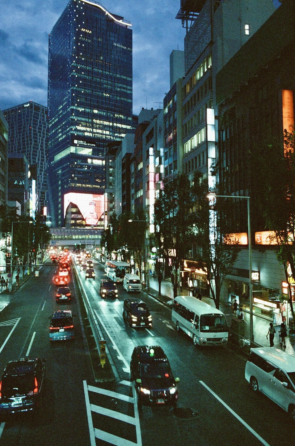 A busy street in Shibuya, Japan, is filled with cars and illuminated buildings at night.