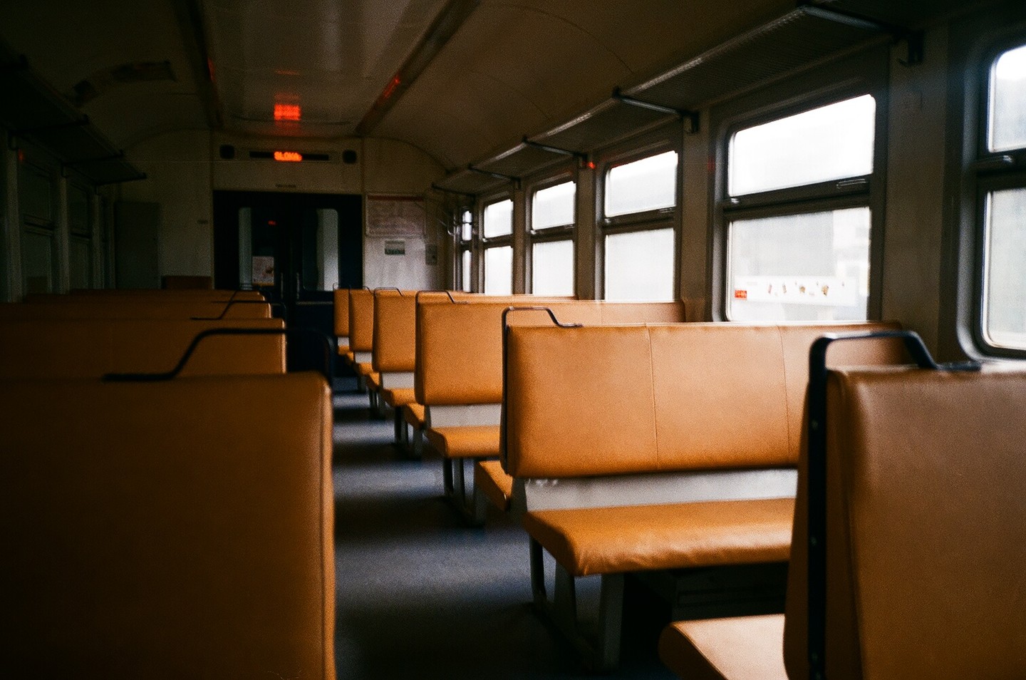 An empty train car with rows of orange seats is illuminated by light from the windows.