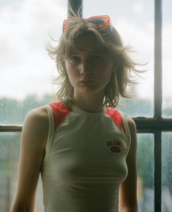 A woman with sunglasses on her head stands in front of a window.